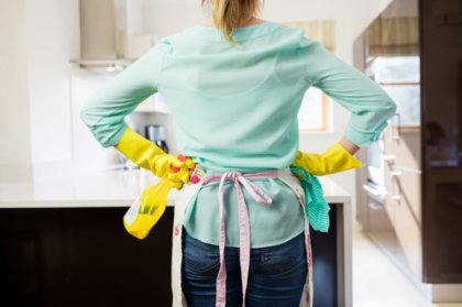 mujer de pie y de espaldas con la botella del aerosol y servilleta en la cocina