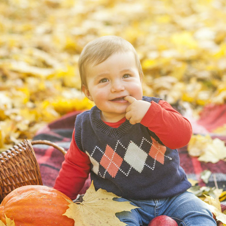 Niño sonriente en una manta encima de hojas de otoño