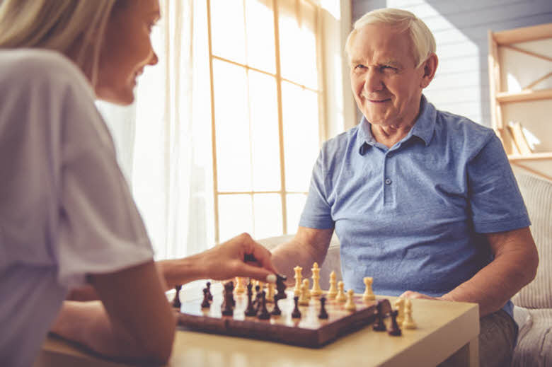 cuidadora de persona mayor jugando ajedrez con un anciano