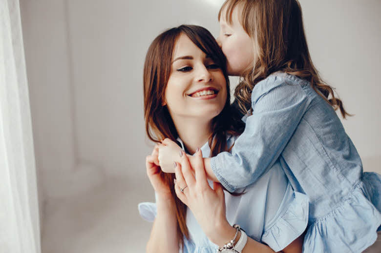 niña abrazando su madre y dándole un beso en la cabeza